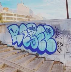 graffiti on the side of a concrete wall with steps leading up to it and buildings in the background