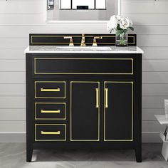 a black and gold bathroom vanity with white flowers in vase next to mirror on the wall