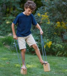 a young boy playing with two wooden blocks in the grass while holding on to ropes