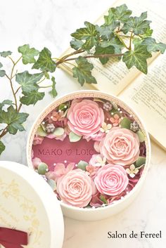 some pink flowers are in a bowl next to an open book