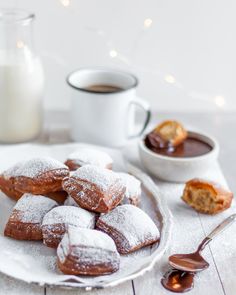 powdered sugar covered donuts on a white plate next to a cup of coffee