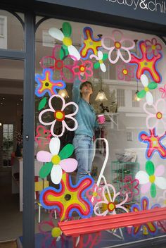 a woman is standing in the window of a shop with flowers and butterflies painted on it