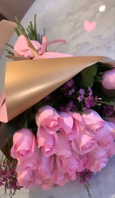 a bouquet of pink roses wrapped in gold paper and tied to a marble counter top