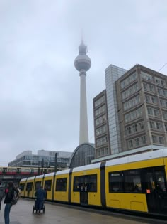 a yellow and white train traveling past tall buildings on a cloudy day in the city