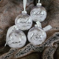 three glass ornaments with names on them sitting on a fur covered surface in front of a blanket