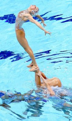 a woman balances on top of another swimmer in the pool