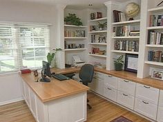 a home office with white bookcases and wooden desk in front of the window