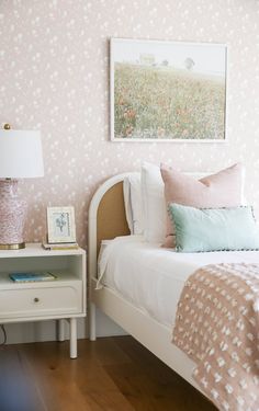 a white bed sitting next to a nightstand with a painting on it's wall