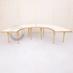 two curved tables with gold legs and white top, against a wallpapered background