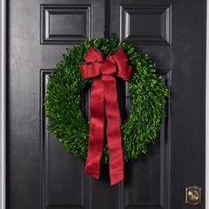 a green wreath with a red bow hanging on the front door to a black door