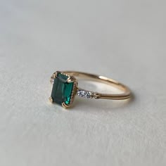 an emerald colored ring with two diamonds on it's sides, sitting on a white surface