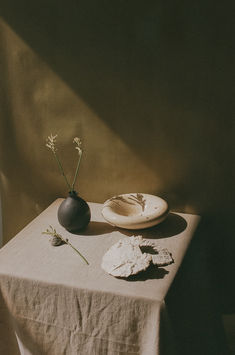 a table topped with a plate next to a vase filled with flowers on top of a table