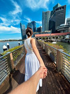 a person holding the hand of another persons hand on a bridge over water with buildings in the background