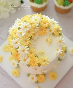 there is a white cake with yellow flowers on it and cupcakes in the background