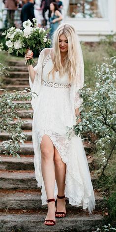 a woman in a white dress is walking down the stairs with flowers on her hand