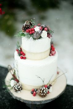 a three tiered white cake with pine cones and berries