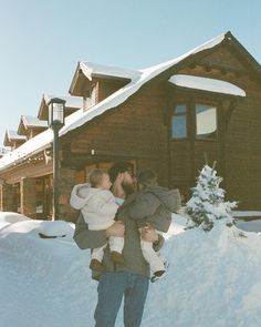 a man and woman kissing in front of a log cabin with snow on the ground