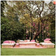 an outdoor seating area with pink cushions and hanging flowers on the tree branches, in front of a lush green lawn