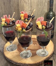 three wine glasses filled with red wine and assorted appetizers on a wooden tray