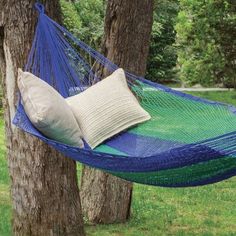 a blue and green hammock hanging between two trees in the grass with pillows on it