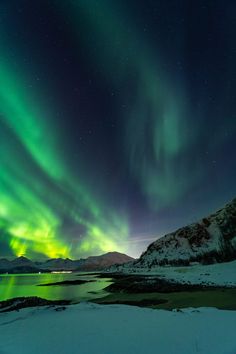 the aurora bore is shining brightly in the night sky over water and snow covered mountains