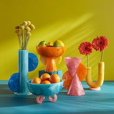 three colorful vases with flowers and fruit in them