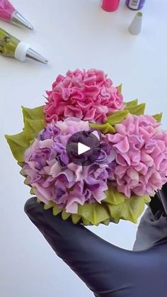 a hand holding a bouquet of flowers on top of a white table next to markers and pens