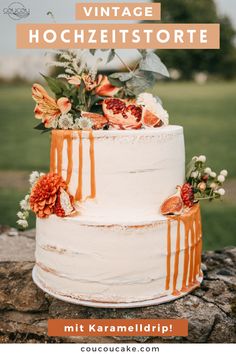 a white cake with orange icing and flowers on top is sitting on a rock