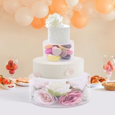 a three tiered wedding cake with flowers on the side and balloons in the background