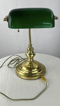 a green table lamp sitting on top of a white cloth covered table next to a charger