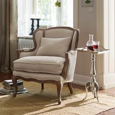 a living room with a chair, table and vase on the floor in front of a window