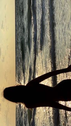 a person standing in front of the ocean with their shadow on the water's surface