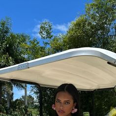 a woman standing in front of a white golf cart with flowers on the side and trees behind her