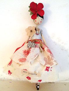 a doll is hanging on the wall with a red flower in it's hair