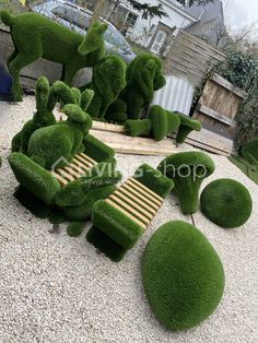 some green grass sculptures sitting on top of a white gravel ground next to a wooden bench