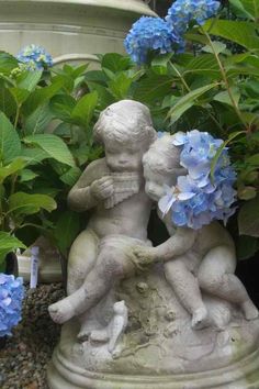 there is a statue of two children holding each other in front of some blue flowers