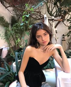 a woman in a black dress sitting at a table with greenery and potted plants