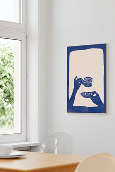 a blue and white painting hangs on the wall next to a table with two chairs