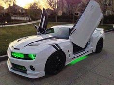 a white sports car with green lights on it's hood is parked in front of a house