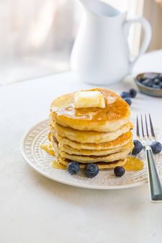 a stack of pancakes with butter and blueberries on a plate next to a fork