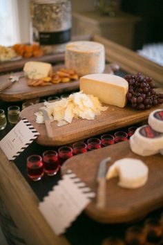 several cheeses and wine are on wooden trays