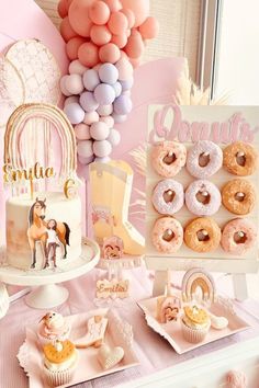 a table topped with lots of donuts next to a cake and balloons in the air