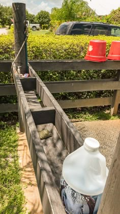 a bottle of water sitting on top of a wooden bench next to a red trash can