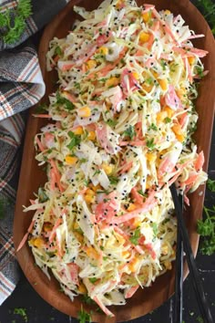 a wooden platter filled with coleslaw salad and two black serving spoons