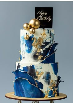 a three tiered blue and white cake with gold decorations on it's sides