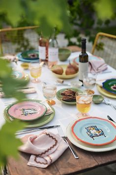 an outdoor table set with plates and wine bottles