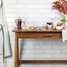 a wooden table topped with lots of food next to a white brick wall and potted plant