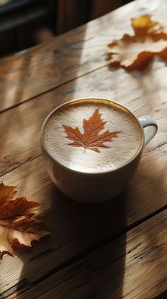 a cappuccino with a maple leaf painted on the side sits on a wooden table