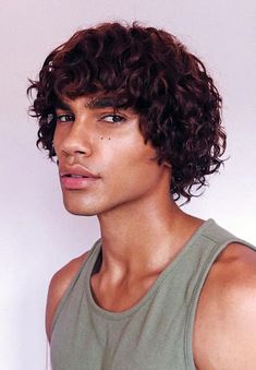 a close up of a person with curly hair wearing a tank top and looking at the camera