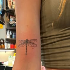 a woman's arm with a small dragonfly tattoo on it